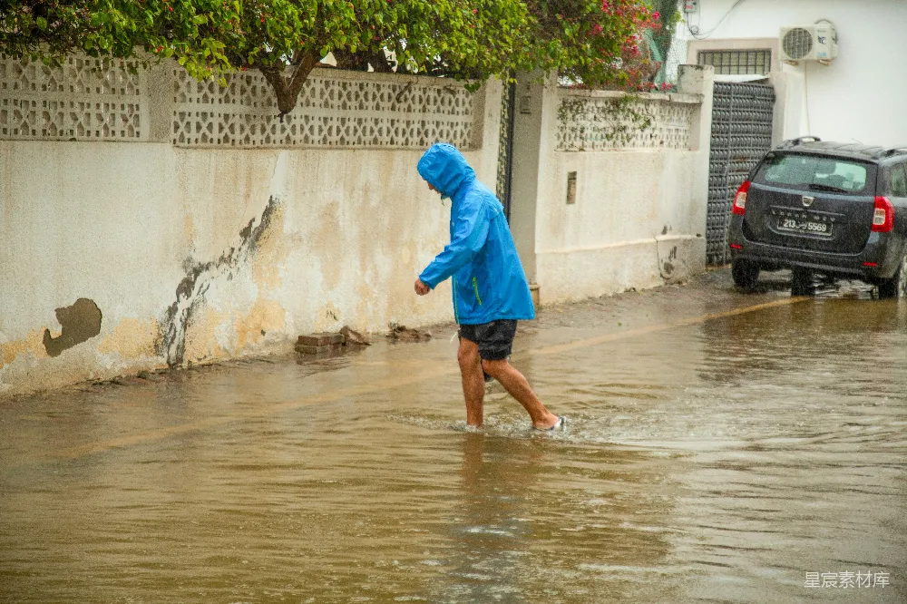 高清摄影 身穿蓝色雨衣的人走在积水的街道上。