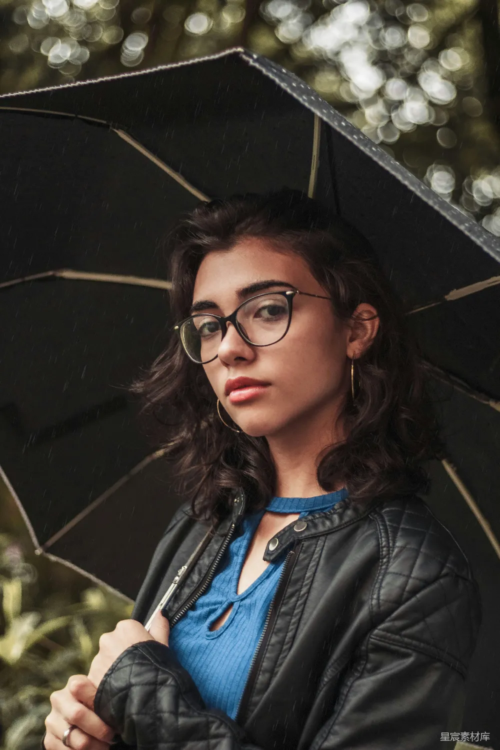 高清摄影 穿着蓝色圆领衫和黑棕色绗缝皮革夹克的女人撑着伞。