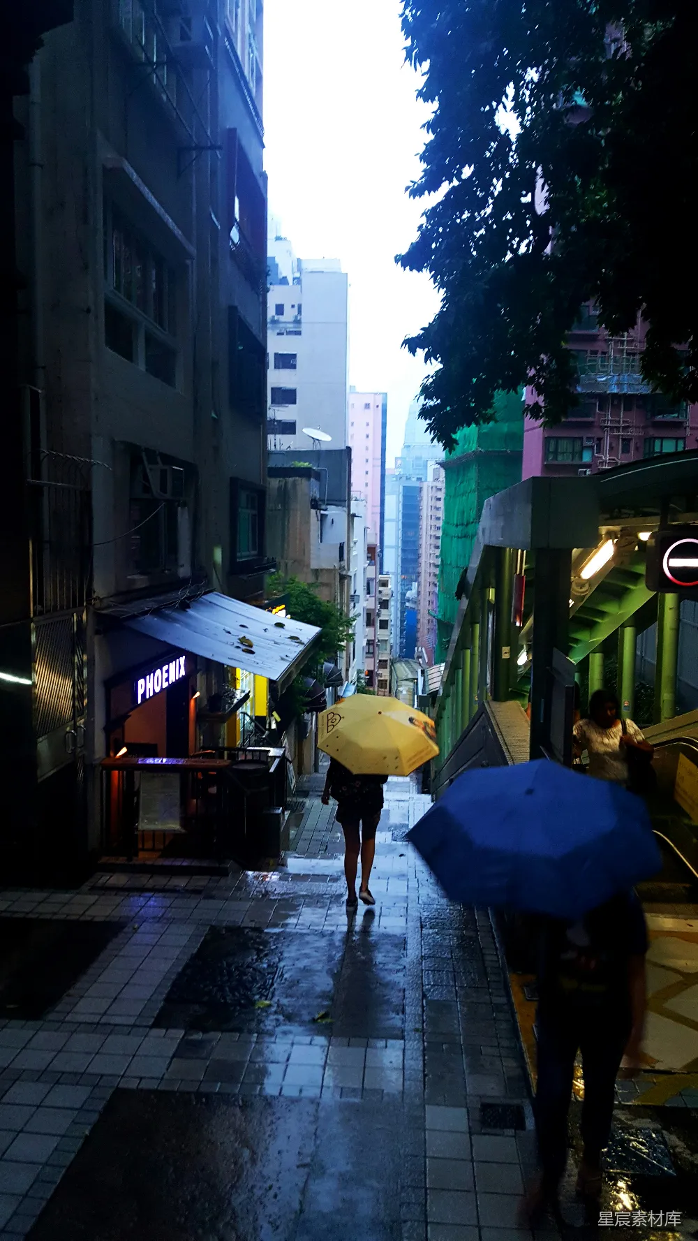高清摄影 街道两栋建筑之间的人们手持蓝色和黄色的伞