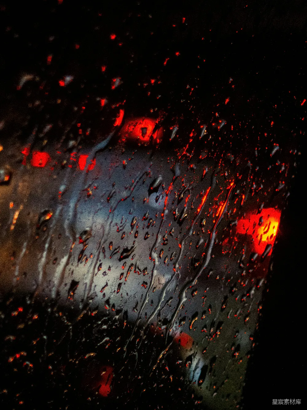 高清摄影 窗外模糊的红灯下，雨滴落在玻璃上。