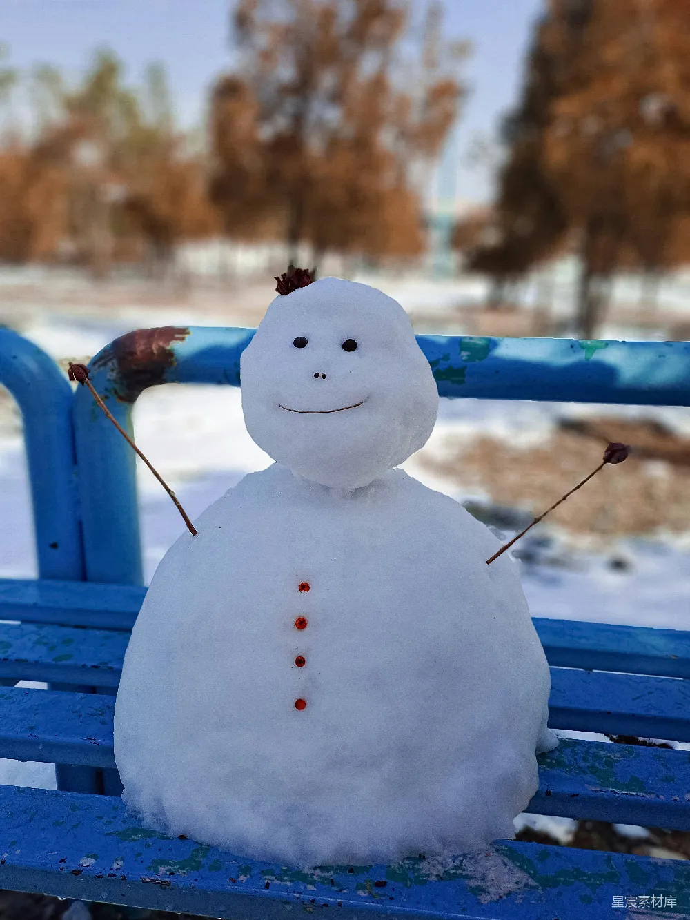 高清摄影 雪人坐在蓝色长凳上，背景是雪地。