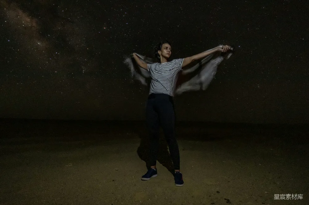 高清摄影 一个男人站在一片沙漠的中央，在满天闪烁着星星的夜空下。