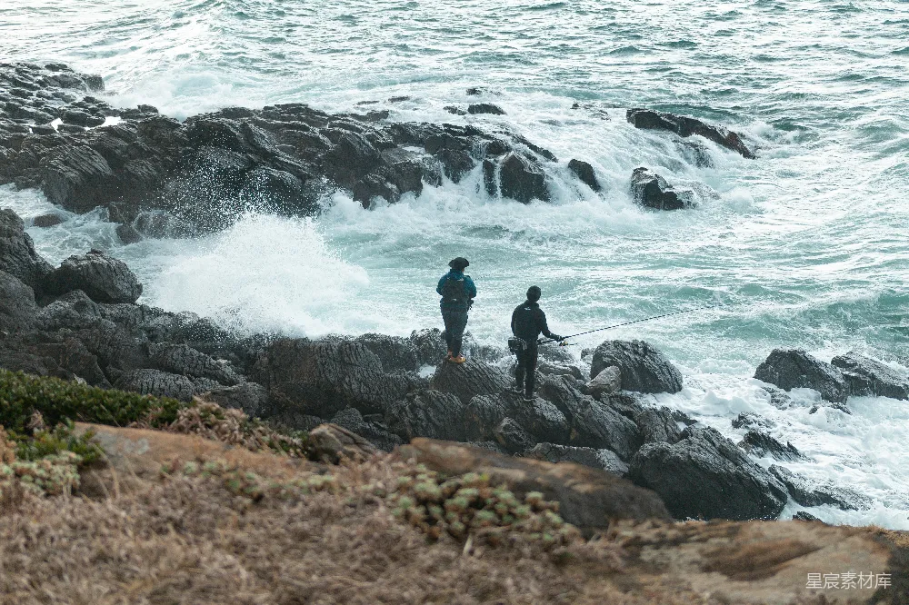 高清摄影 黑色夹克的男人站在海边岩石上，白天靠近海浪。