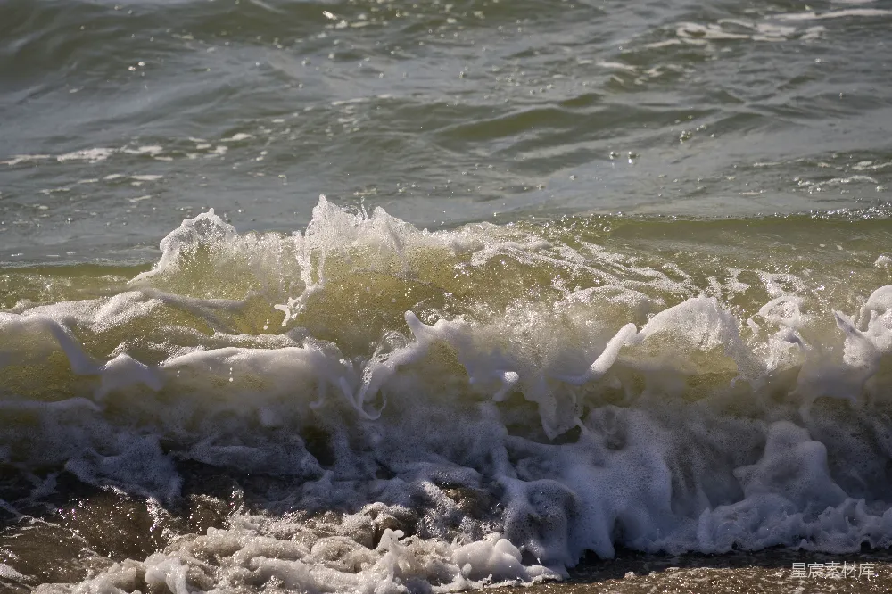 高清摄影 海浪拍打在岸边，泛着白色的泡沫。