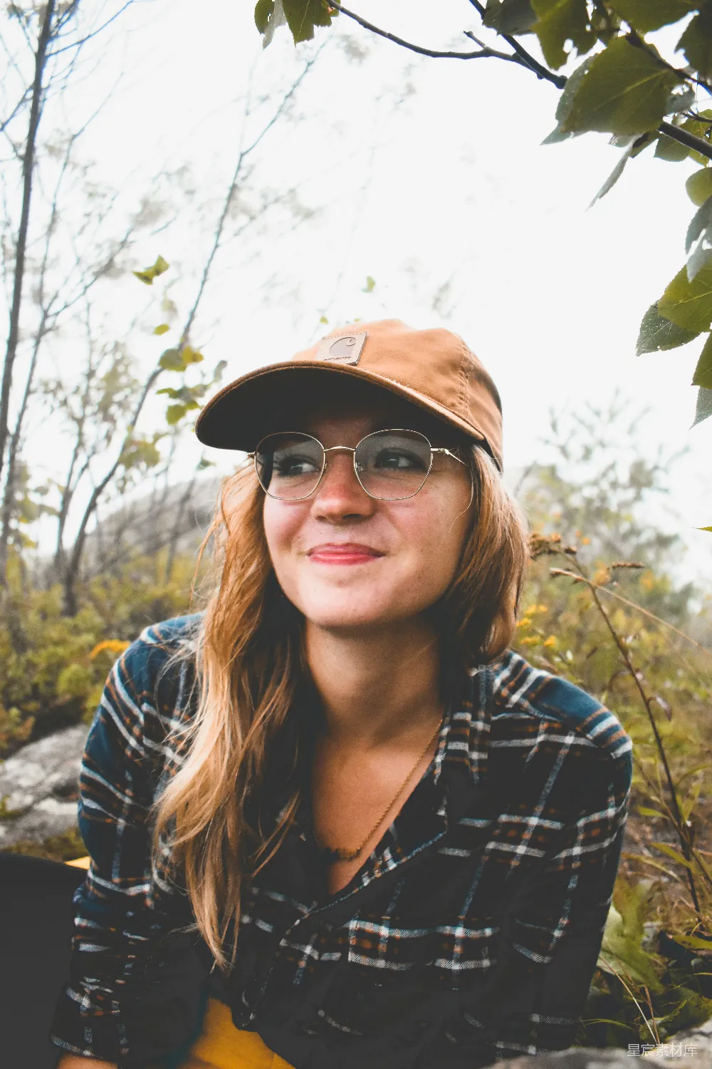 高清摄影  一个戴着帽子和眼镜的女人坐在一块岩石上。