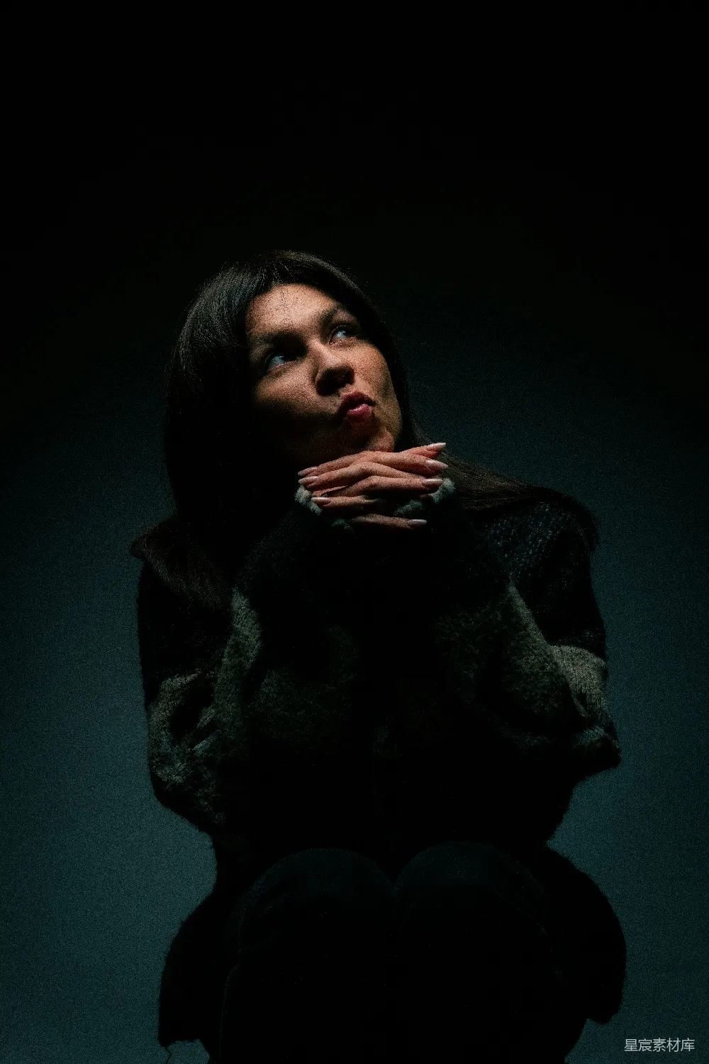 高清摄影  一个女人坐在黑暗中，双手放在胸口。