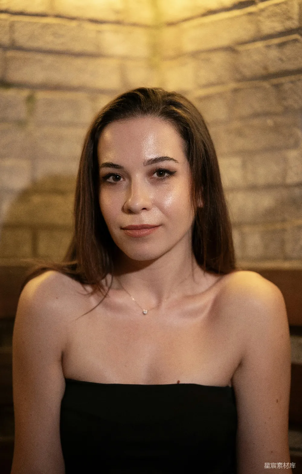高清摄影 黑 top 穿着的年轻女子靠在温暖的红砖墙上。