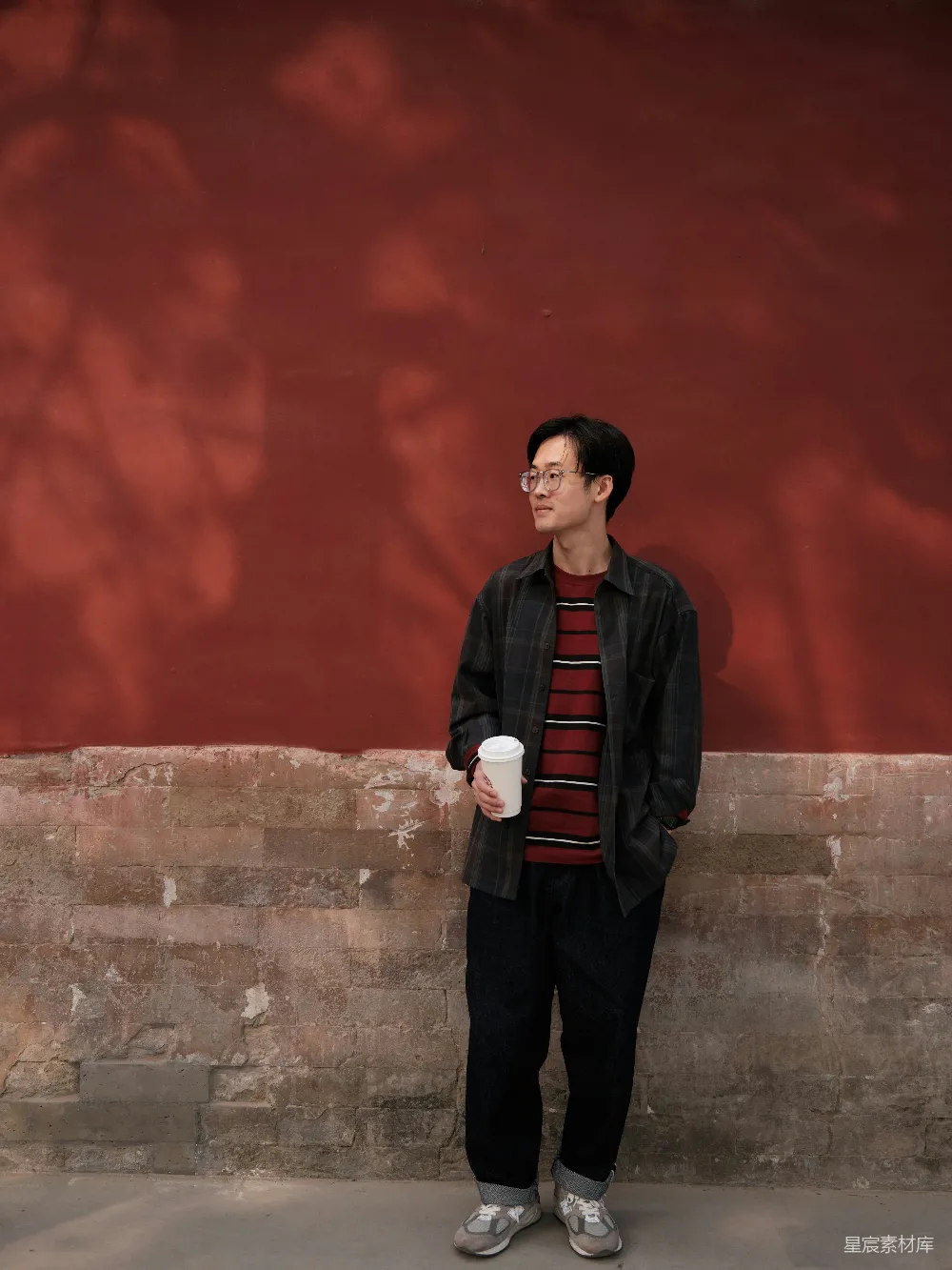 高清摄影 一个男子站在墙边拿着一杯咖啡。