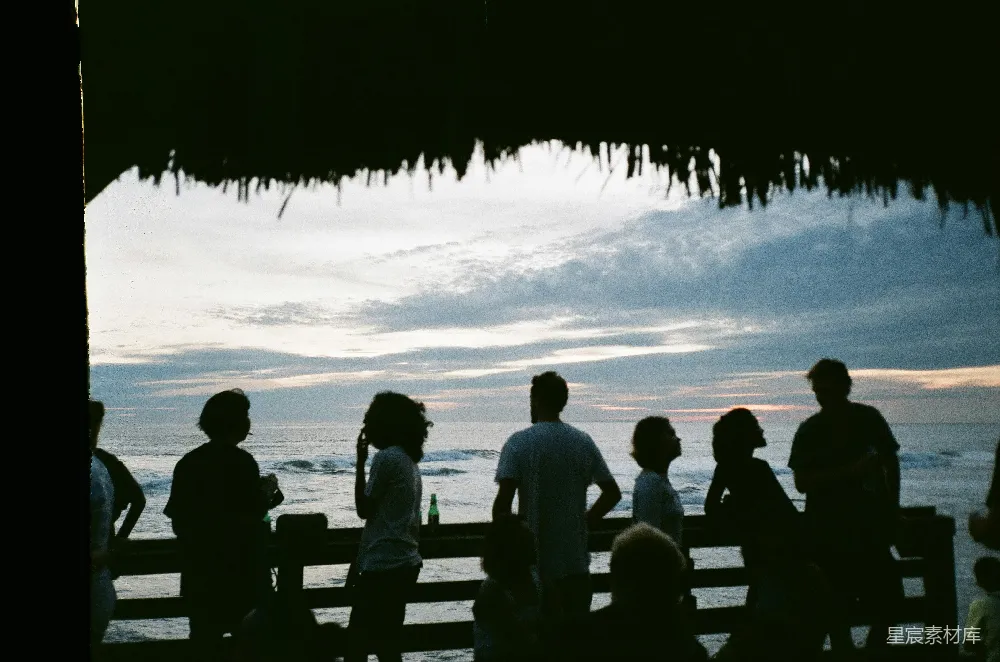 高清摄影 海边傍晚时分人们坐在木制长椅上的情景