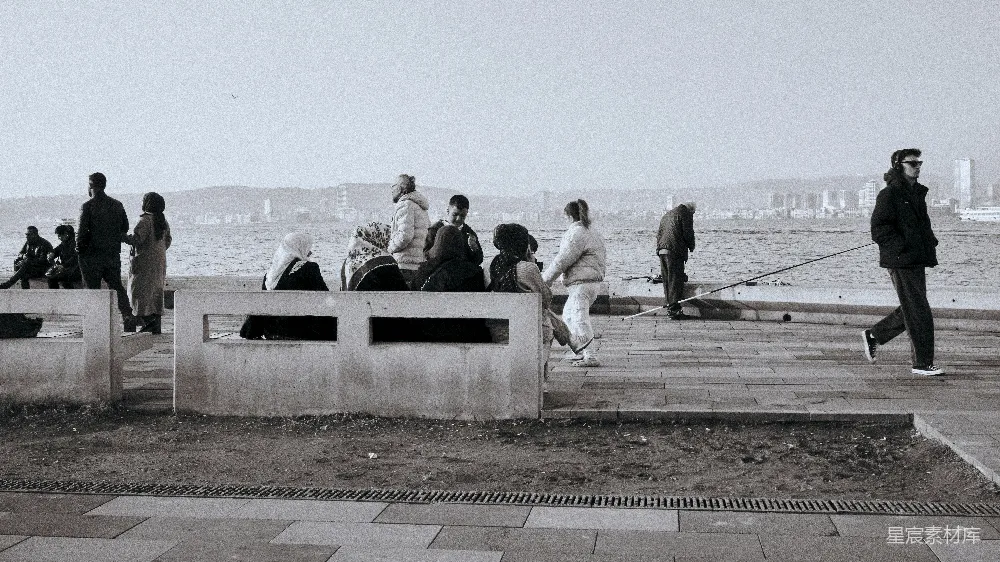 高清摄影  人们聚集在一条 waterfront promenade 上，周围是城市 skyline。