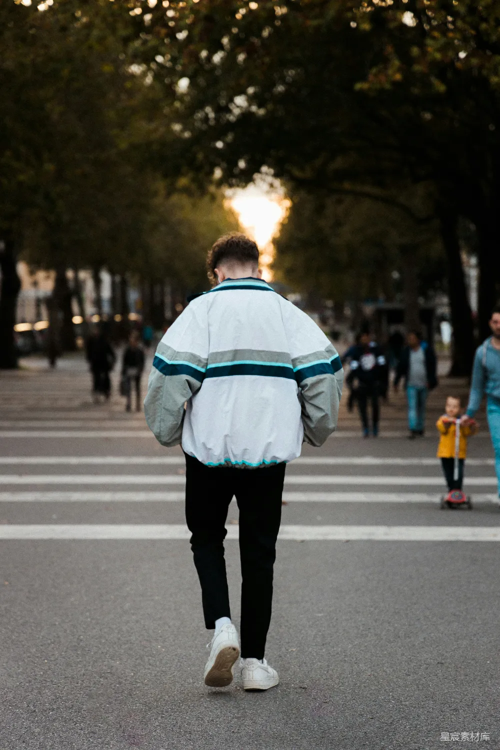 高清摄影 身穿白色和蓝色夹克、黑色牛仔裤的男人在街上行走。