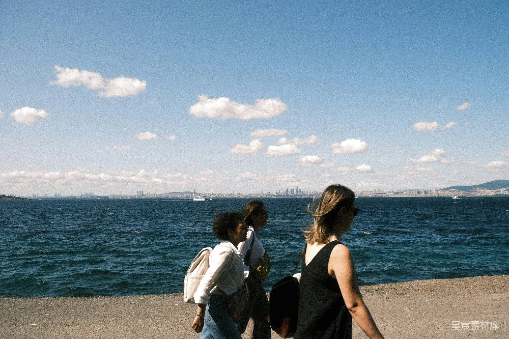 高清摄影 三人沿着 waterfront 走着，天空是蓝色的。