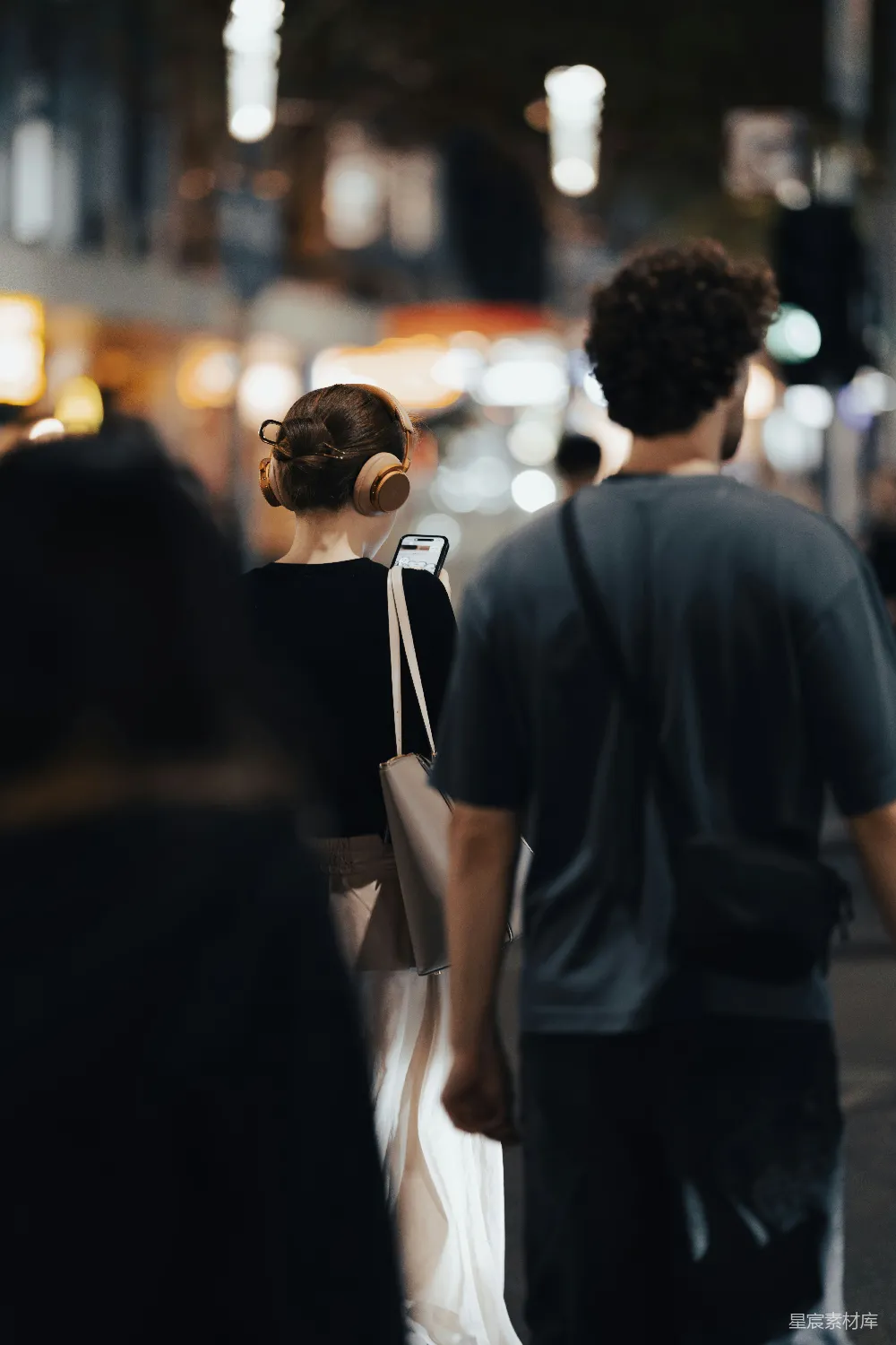 高清摄影  戴着耳机的女人和一个男人走在城市街道上。