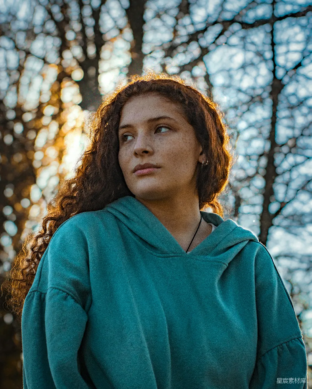 高清摄影 一个穿着绿色风衣的女人站在树前。