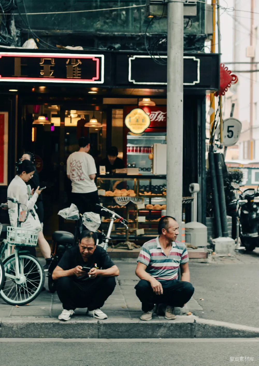高清摄影 两名男子蹲坐在商店外的 sidewalk 上。