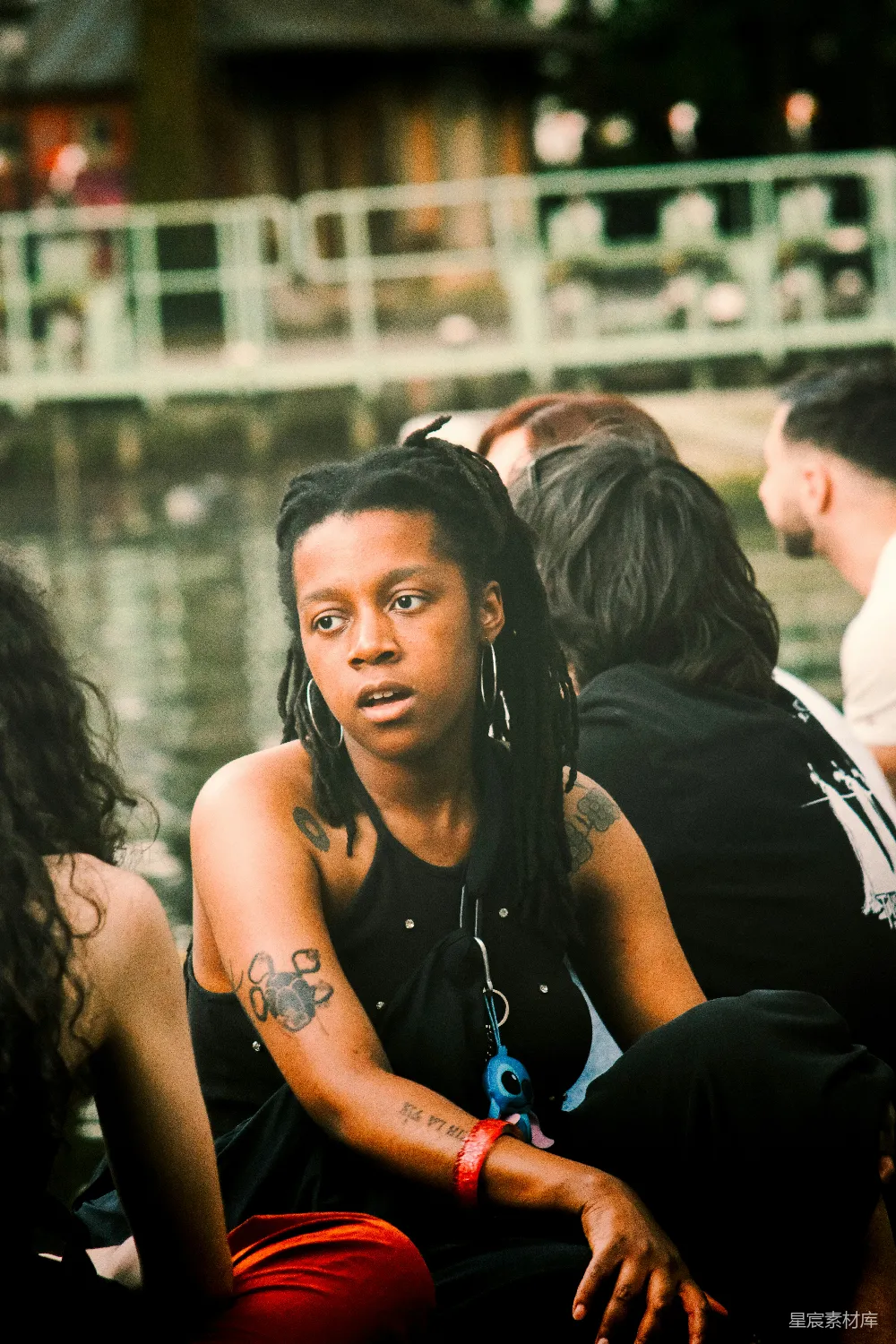 高清摄影 一个头缠 dreadlocks 并有文身的女性坐在户外靠近水边。