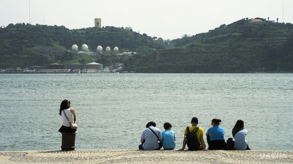 高清摄影 人们在水边放松，远处有山和建筑。