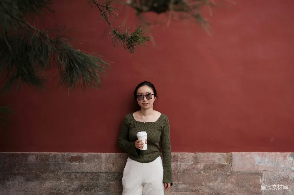 高清摄影 人物 一位女性倚靠在墙上，手中拿着一杯咖啡。