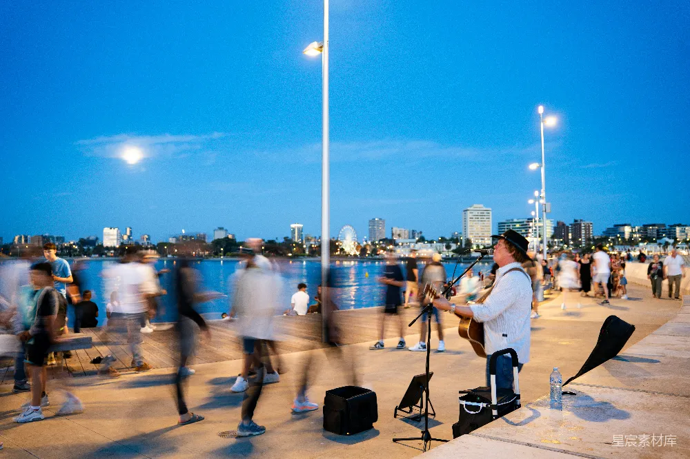 高清摄影 音乐人在黄昏时分的 waterfront promenade 上弹奏吉他。