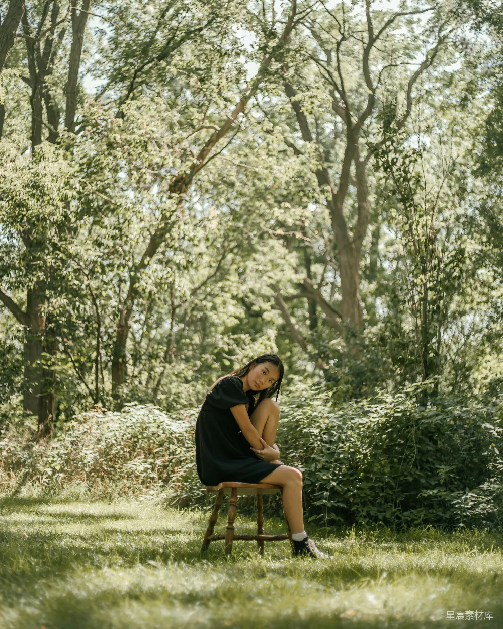 高清摄影 黑色上衣的女人坐在棕色木椅上，下面是一片绿色的树林，在白天。