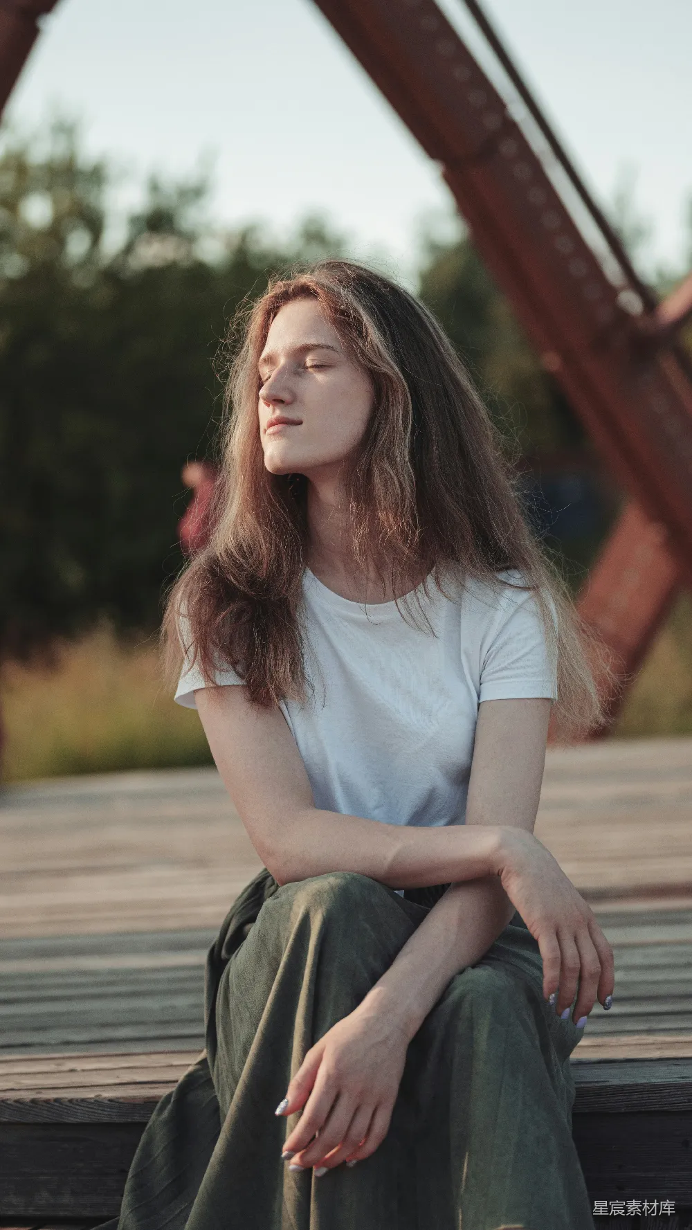 高清摄影 人物 白色长袖圆领T恤的女人在木质桥上白天坐着，桥是棕色的。