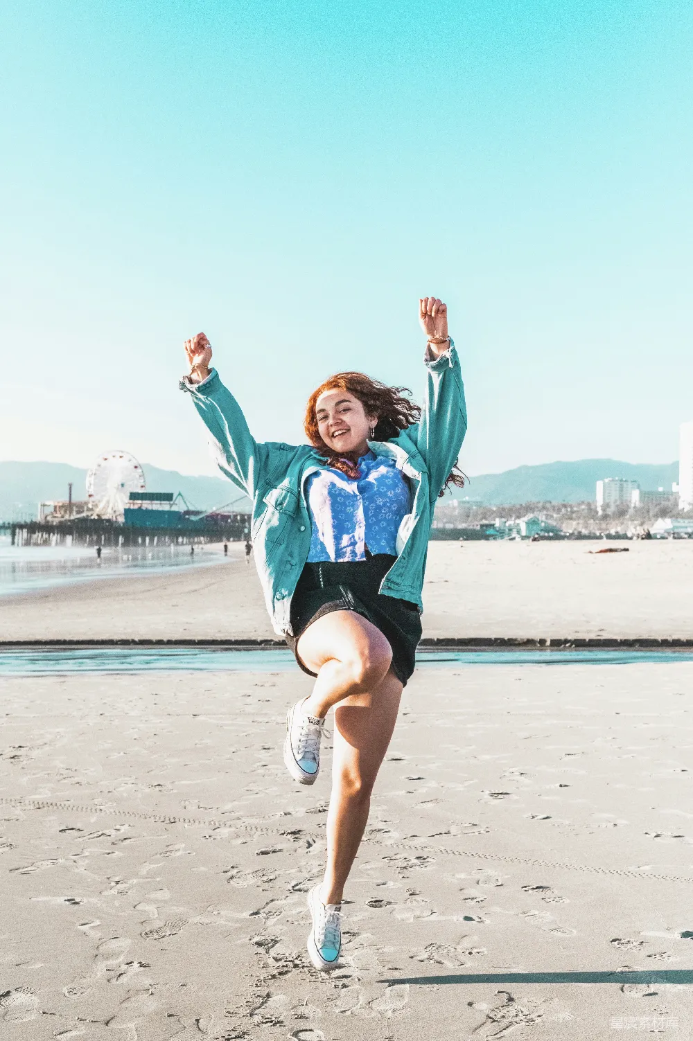 高清摄影  蓝夹克女人穿着黑色短裤在白天海滩上跳跃