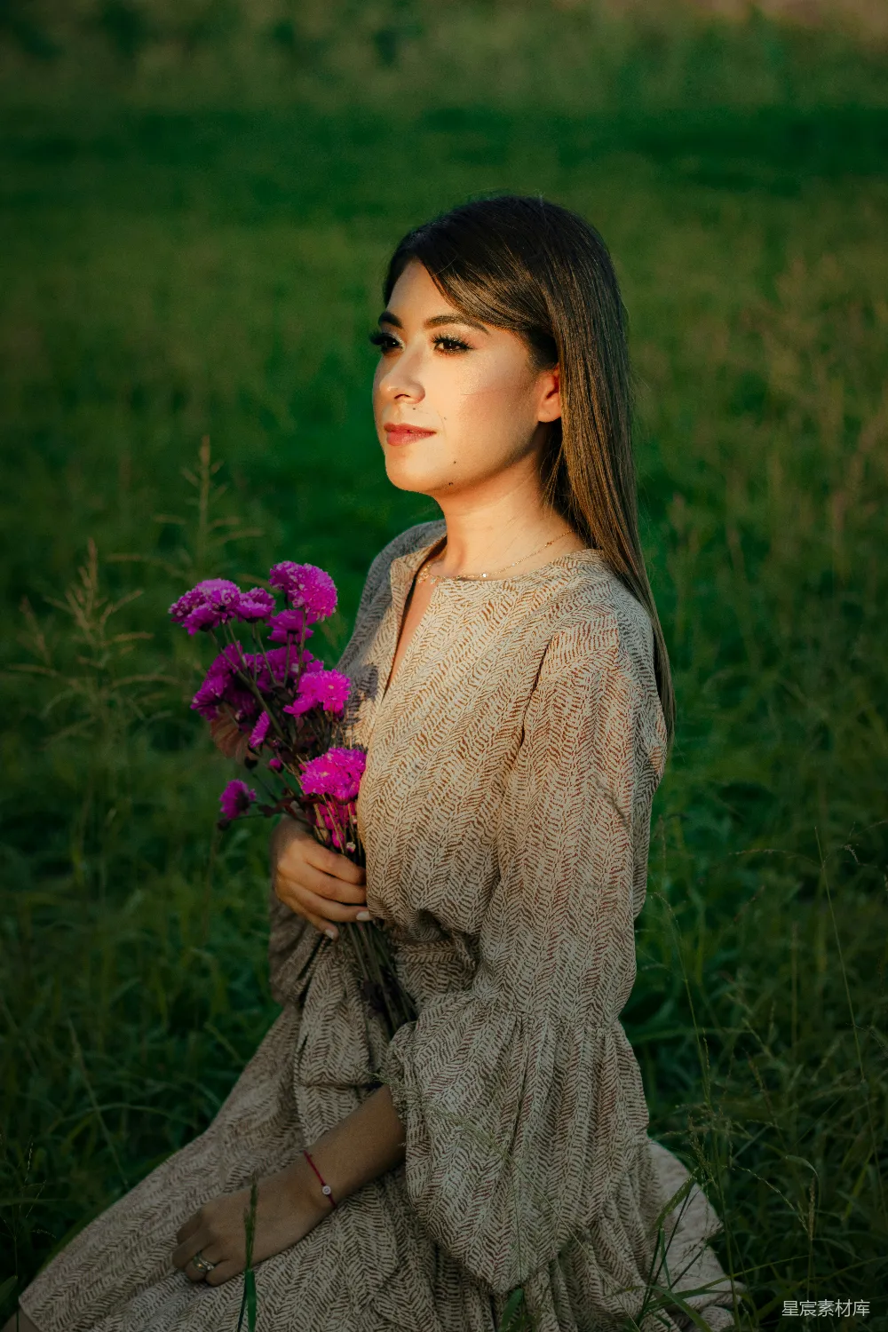 高清摄影  一个女人坐在田野里，手中拿着一束花。