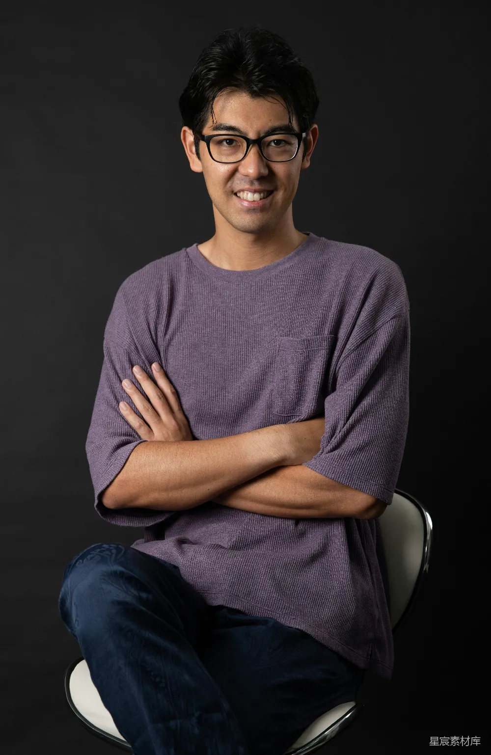 高清摄影  灰tee恤着装的男人坐在黑色的椅子上，穿着蓝色的牛仔裤。
