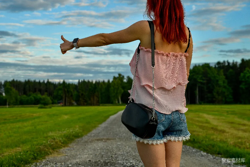 高清摄影  红发女子在乡村小路上 hitchhiking。