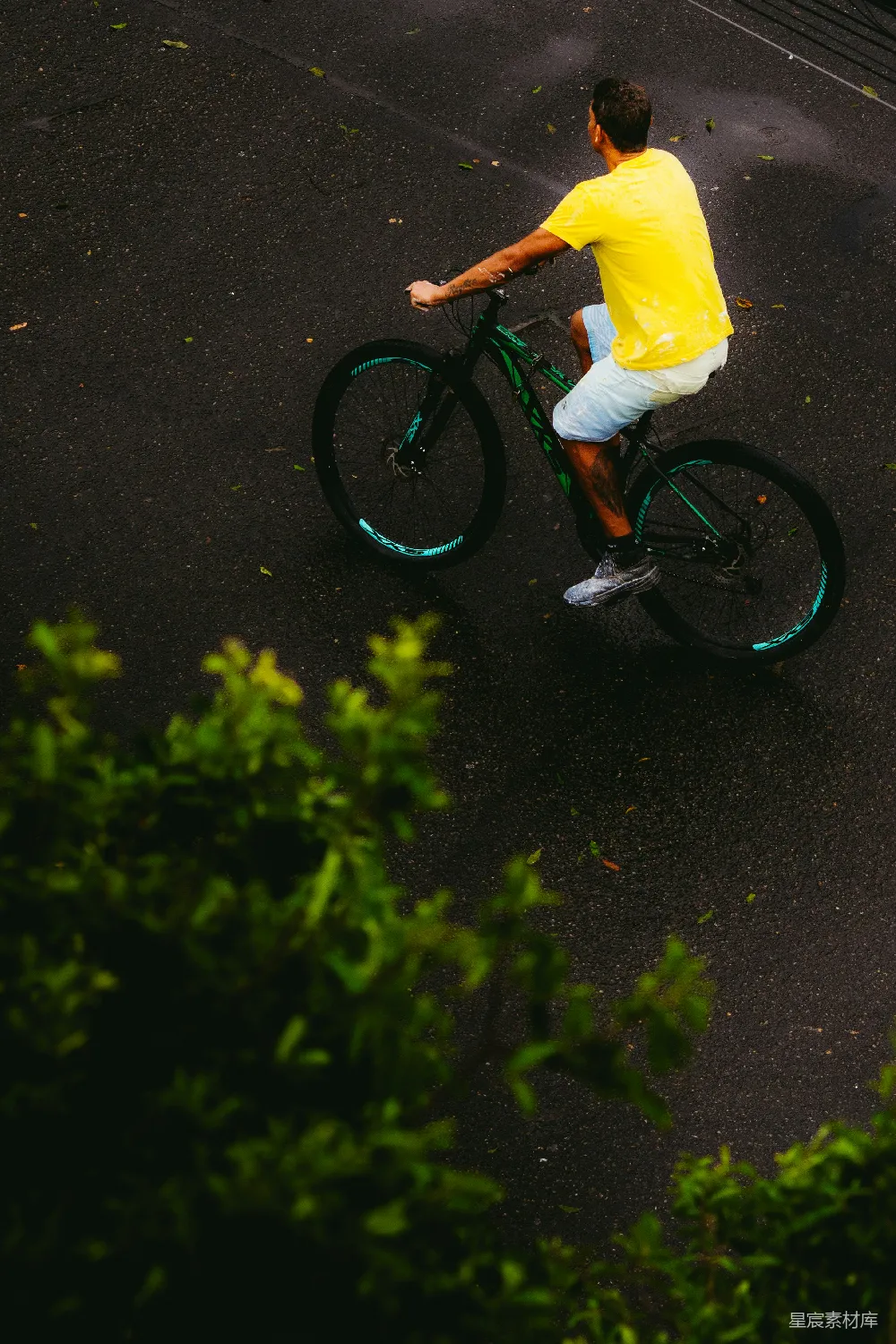 高清摄影  穿黄衬衫的男人在湿路上骑自行车。