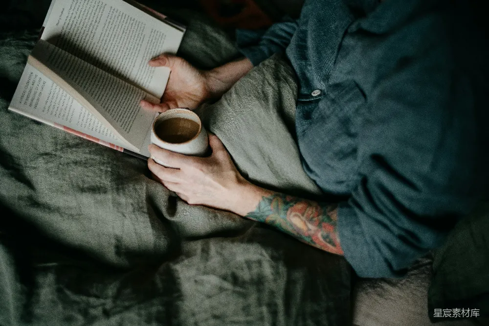 高清摄影  一个人在床上躺着，旁边有本书和一杯咖啡。