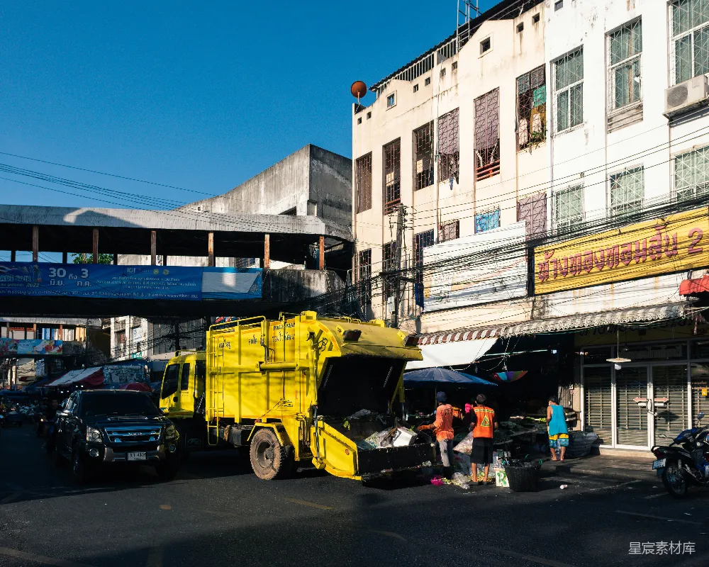 高清摄影  一辆黄色的垃圾 truck 停在了一栋建筑前面。