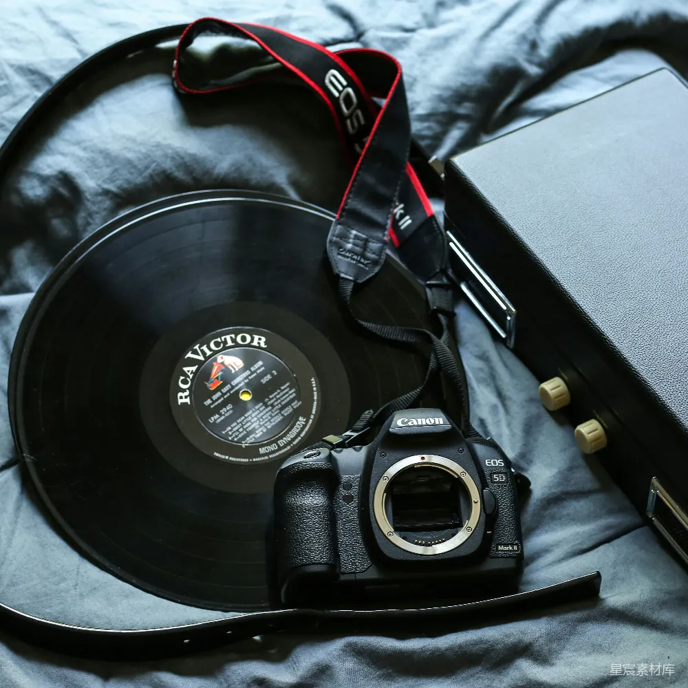 高清摄影  黑色的佳能EOS 5D DSLR相机旁边有一个黑色的 RCA Victor 胶片唱片。