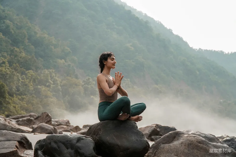 高清摄影  一个女人坐在一块岩石上，旁边是条河。