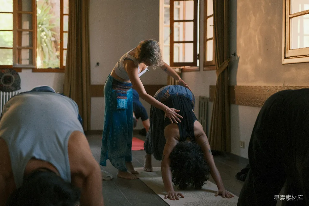 高清摄影 瑜伽教练正在帮助学生做 downward dog 姿势。