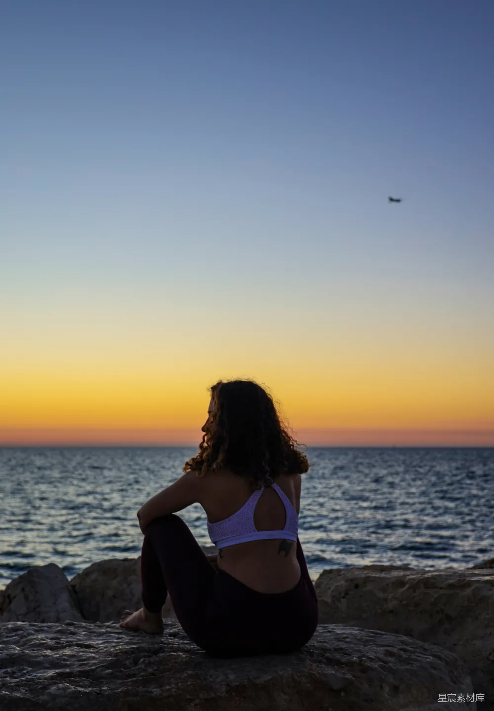 高清摄影 夕阳西下时，女人坐在岩石上面向大海。