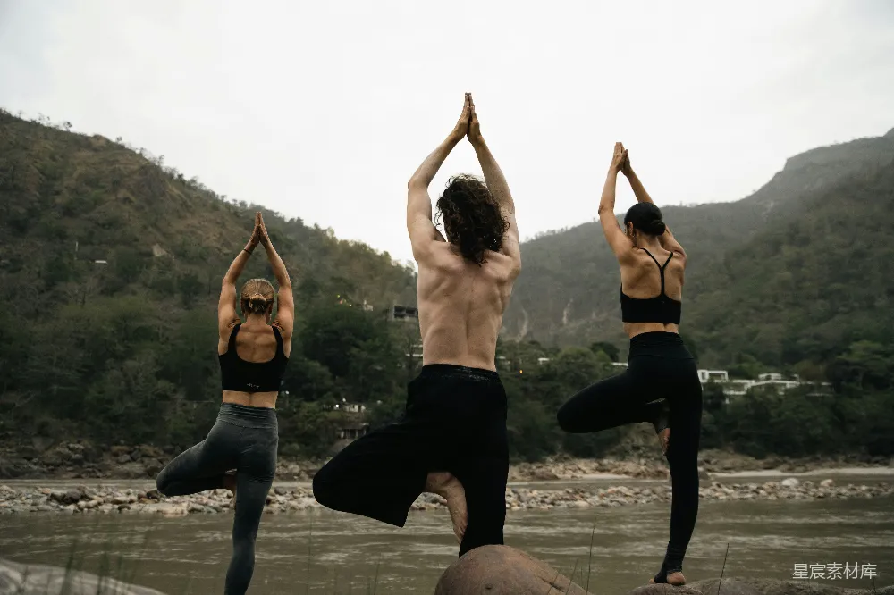 高清摄影  三人在河边一块岩石上做瑜伽