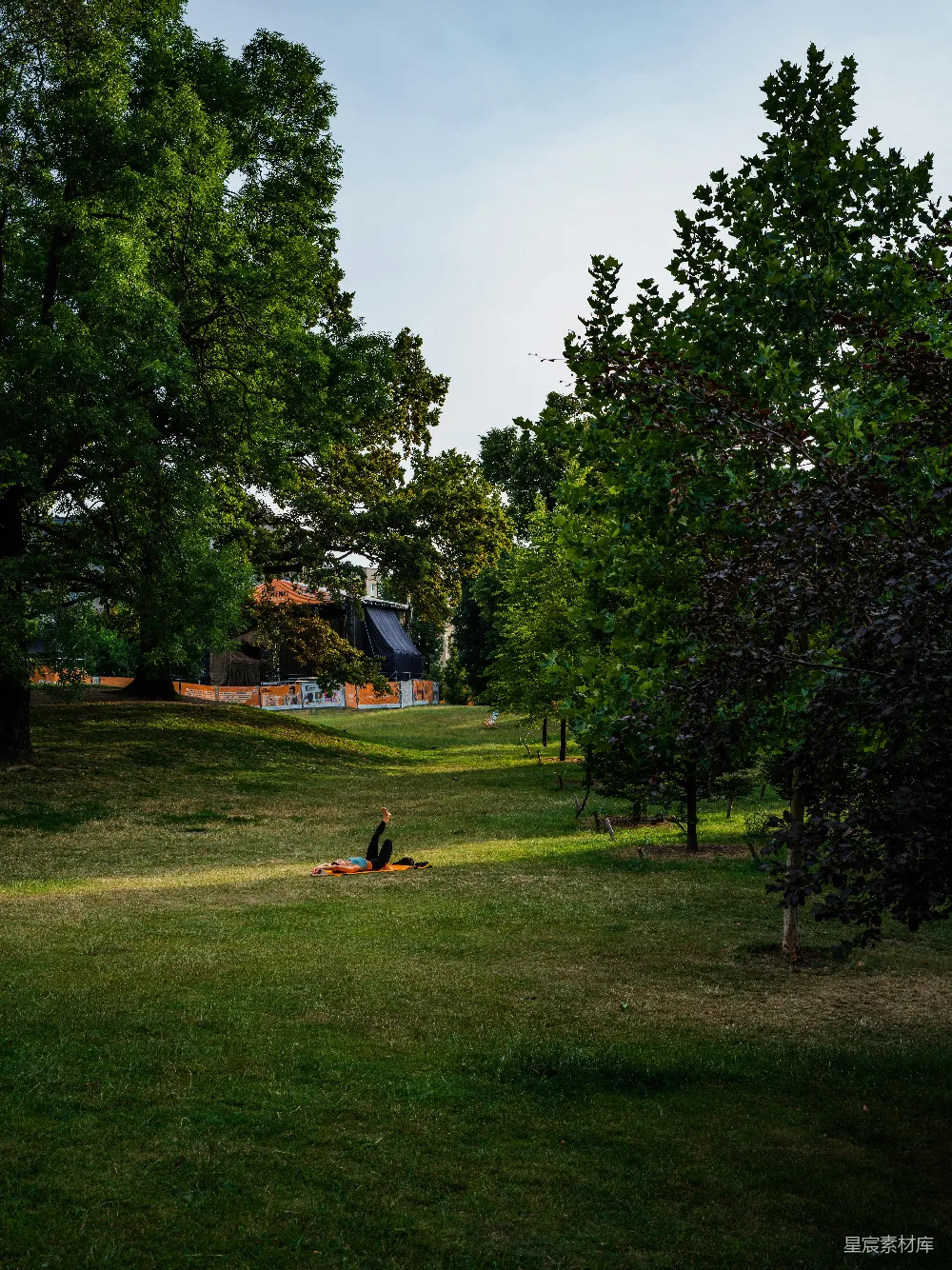 高清摄影 草地上一个躺在毯子上的身影，背景有树木和一座建筑。