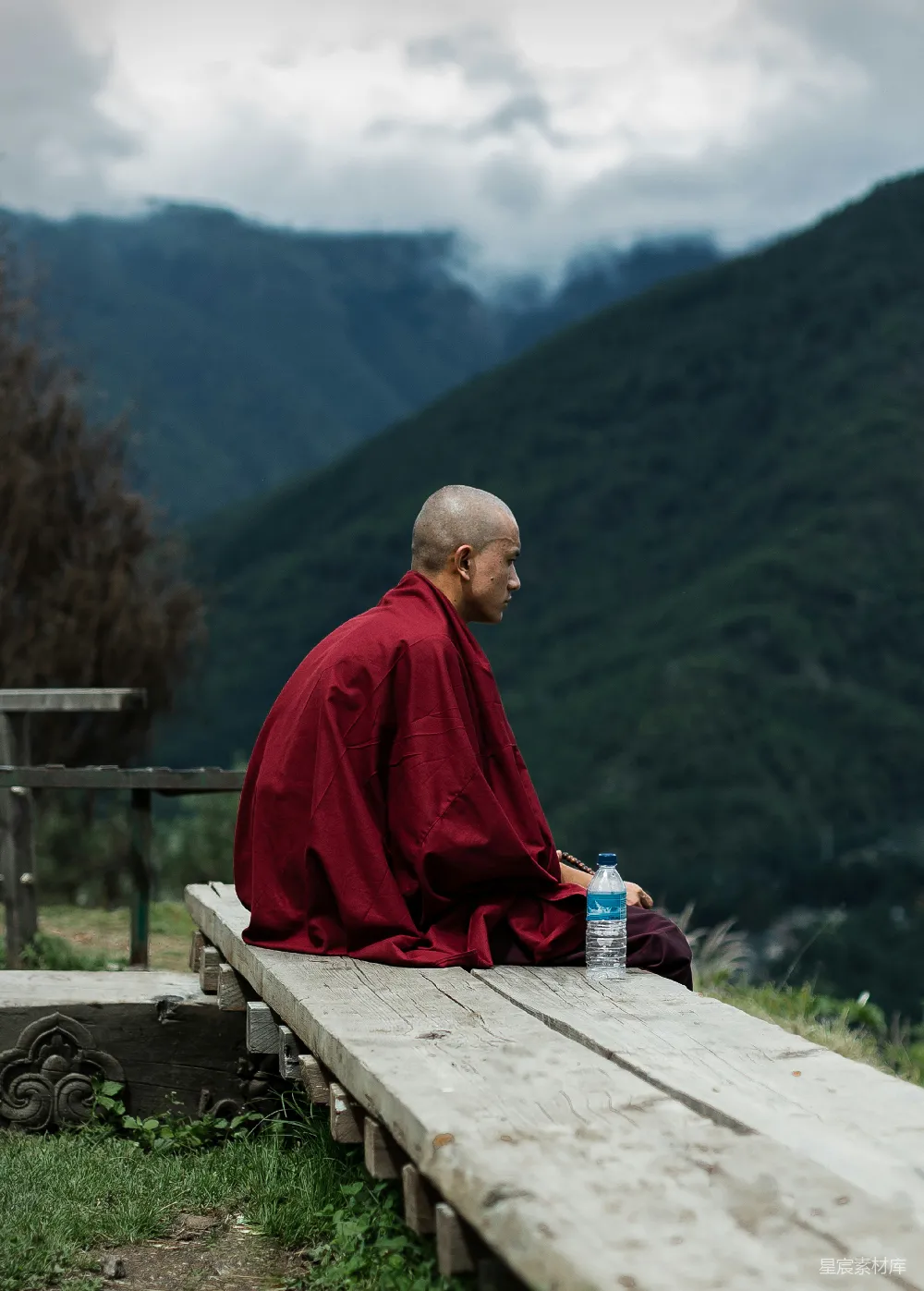 高清摄影 红袍男子坐在棕色木凳上，白天望着绿色的山峦。