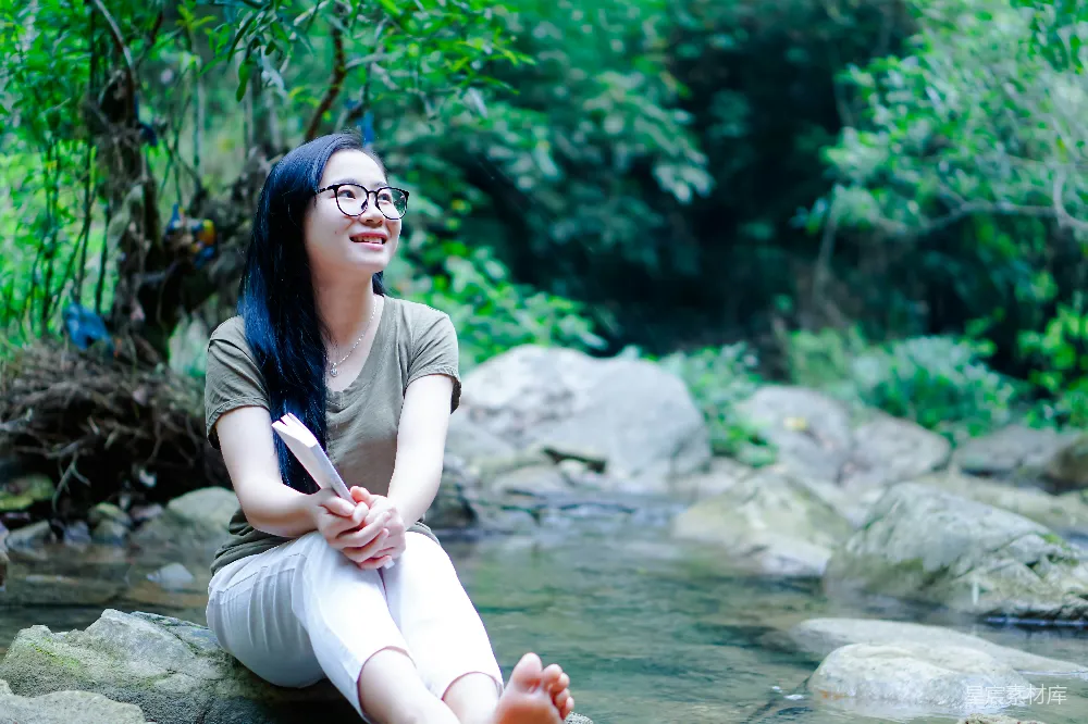 高清摄影 一个女人坐在溪流边的一块岩石上