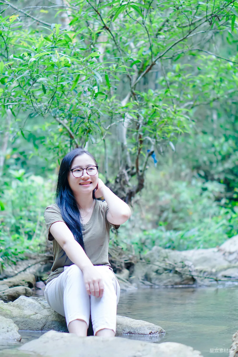 高清摄影 一个女人坐在河边的一块岩石上。