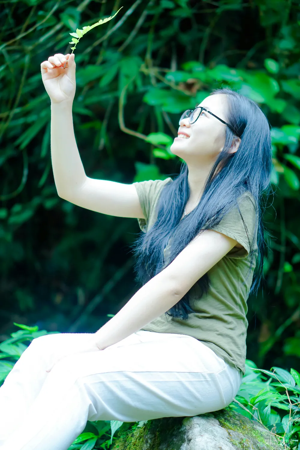 高清摄影 一个女人坐在岩石上，手里拿着植物。