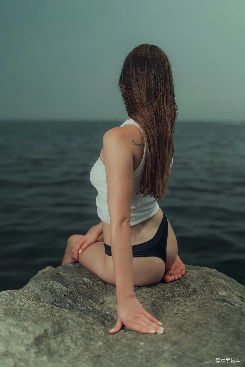 高清摄影  一个女人坐在岩石上，旁边是海洋。