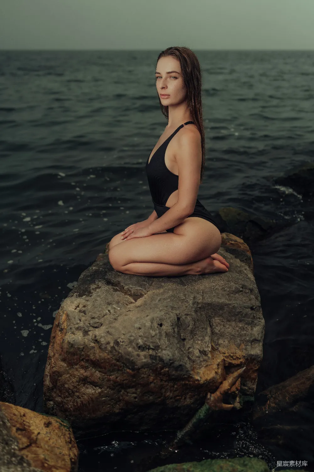 高清摄影 一位女性坐在岩石旁的水边。