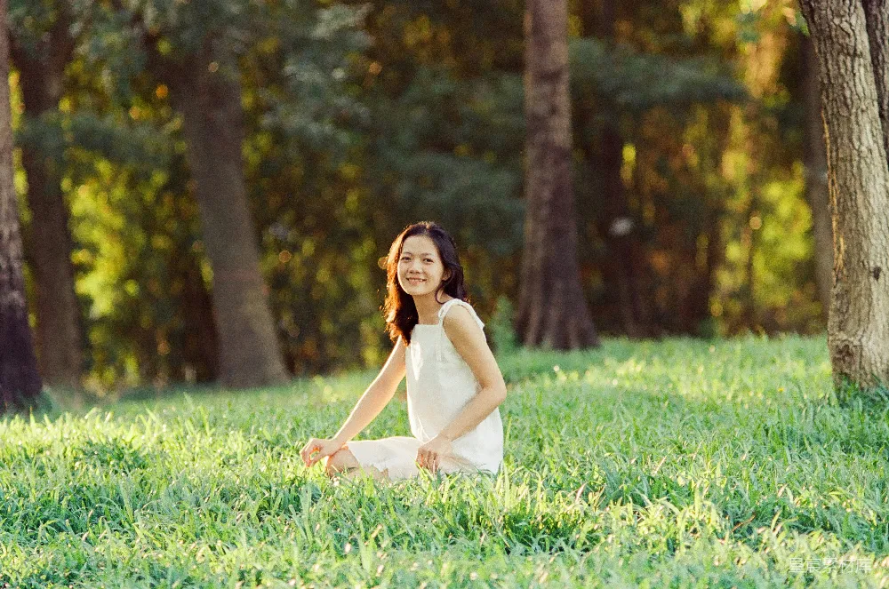 高清摄影 一个穿白色连衣裙的女子坐在草地上。
