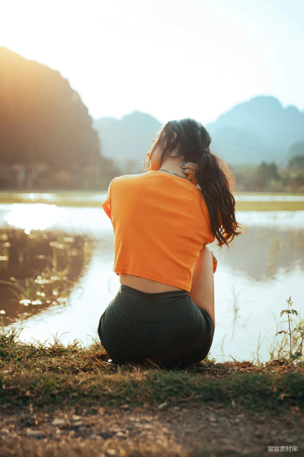 高清摄影 女人坐在水边，背景是山。
