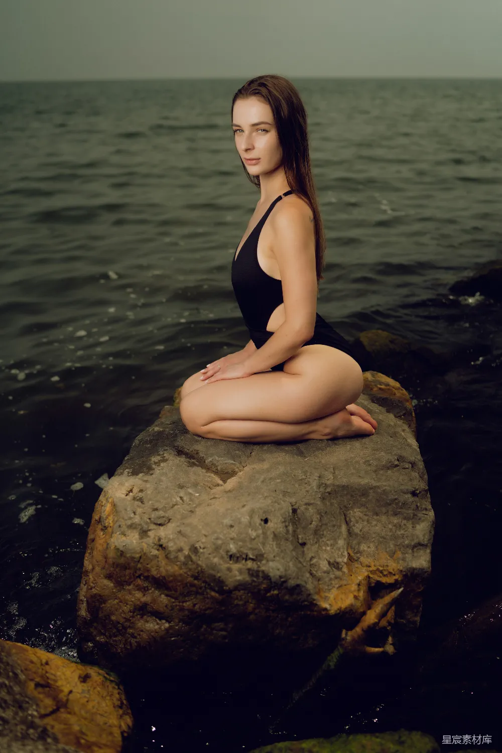 高清摄影 一个女人坐在岩石旁的水边。