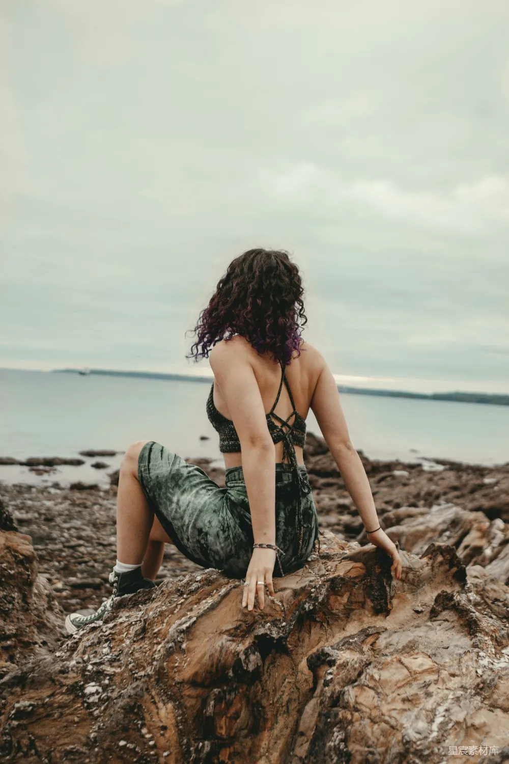 高清摄影 一个女人坐在岩石上，旁边是大海。