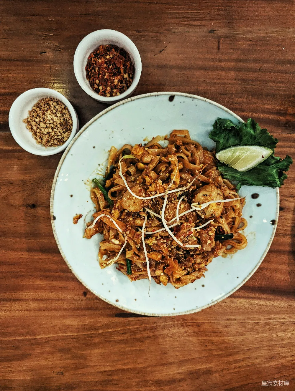 一份放在木质复古餐桌上的pad thai，配以花生碎和辣椒 flakes