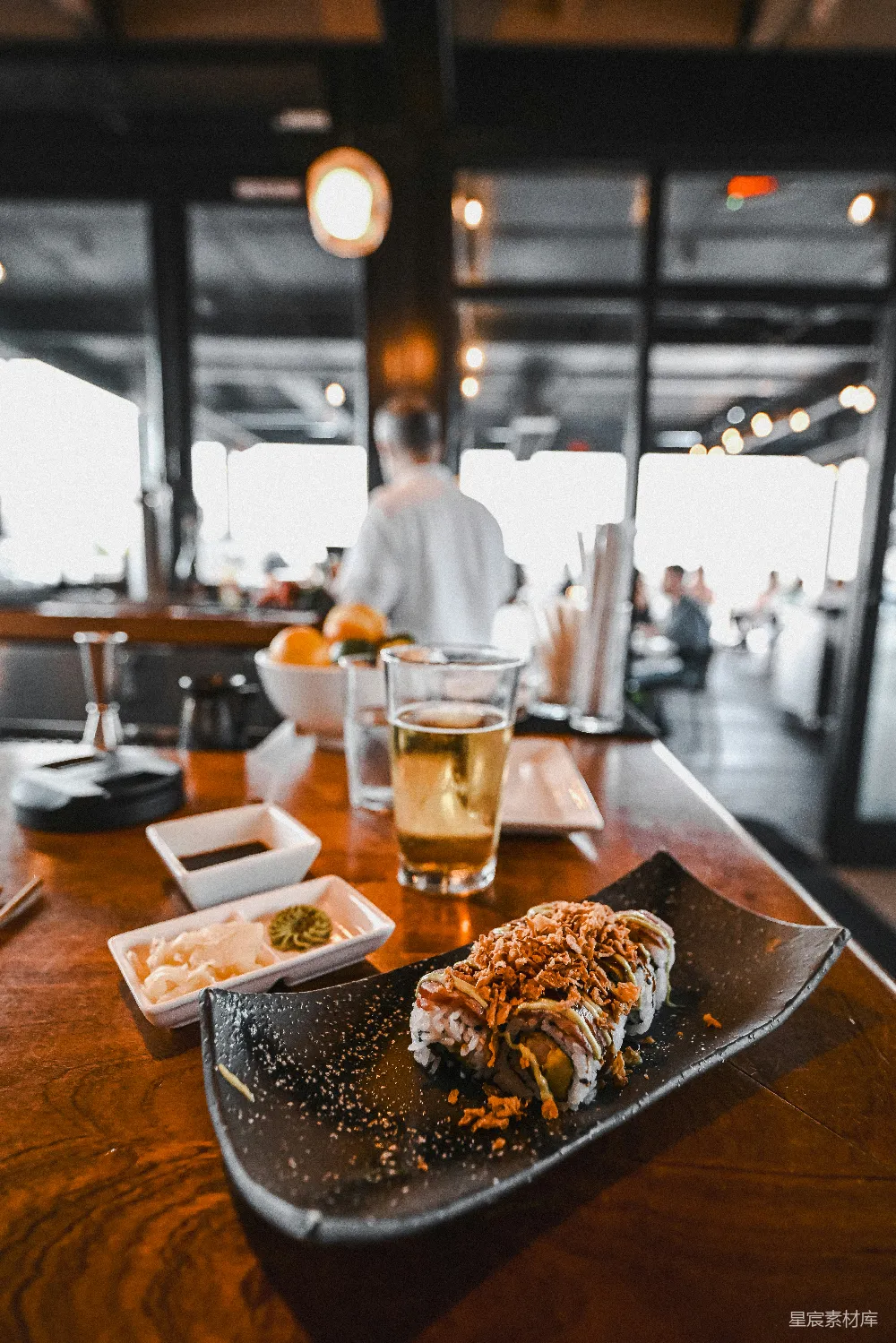高清摄影  寿司卷、酱料和啤酒放在一块暗色木桌上。
